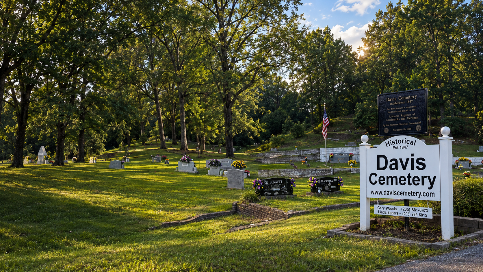 A panoramic view of Davis Cemetery with its historic entrance sign, American flag, mature trees, and hillside graves